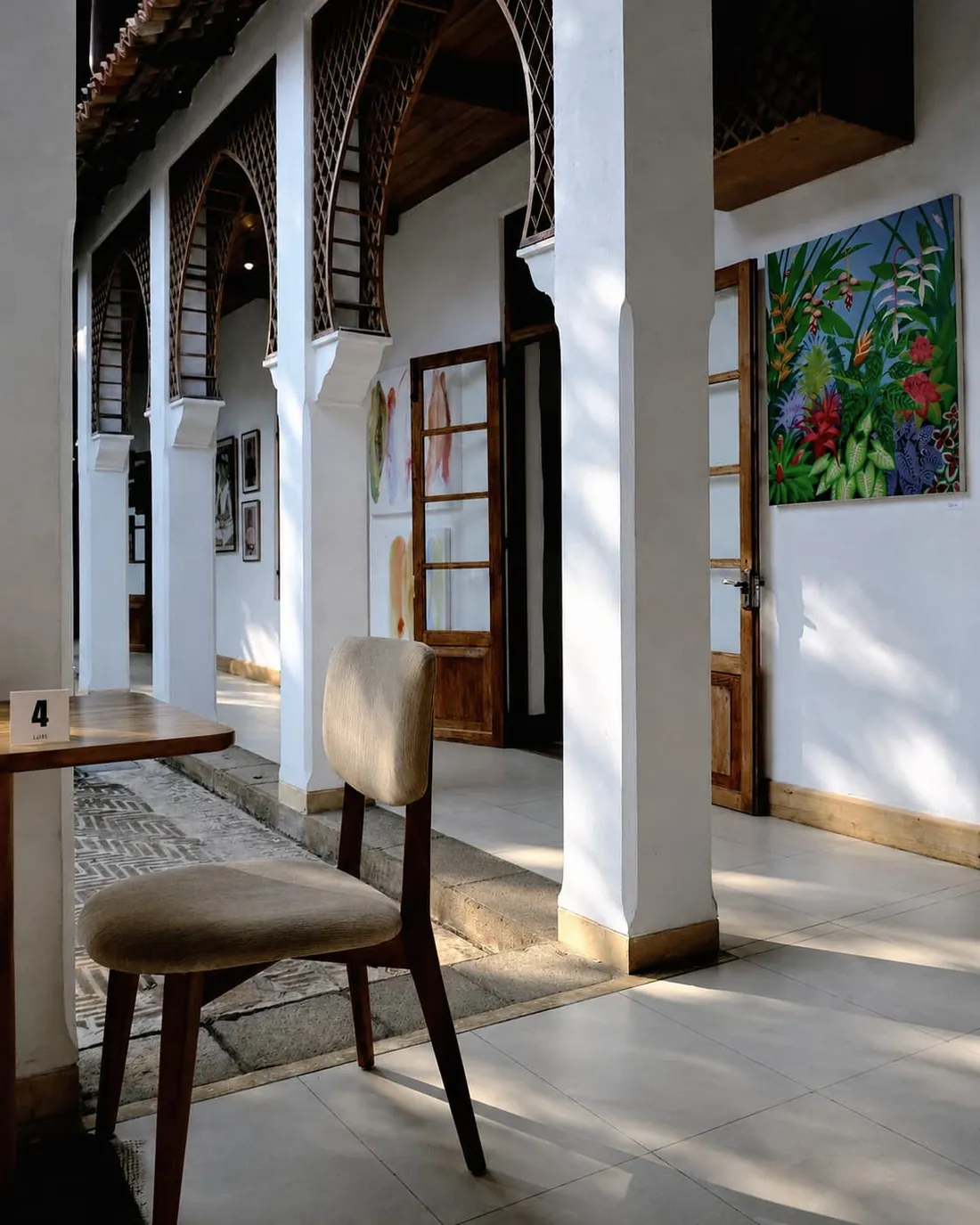 A table and chair on the verandah at Kaffi Galle Fort, paintings on the whitewashed wall behind.